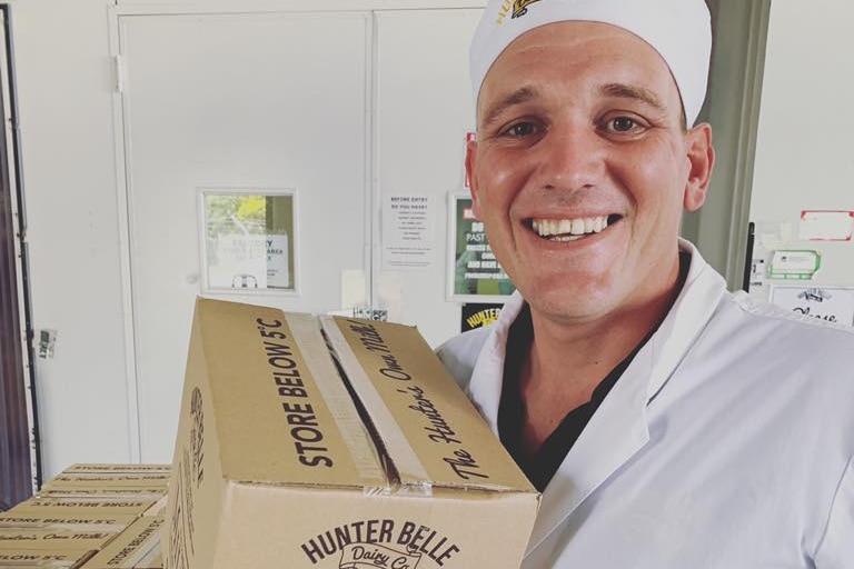 A man in a white coat and hat holds a box of 2 litre milk bottles. He is smiling.
