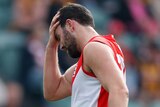 A Sydney Swans AFL player holds his head after being concussed in a match.