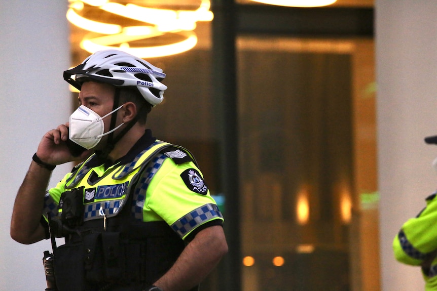 A police officer wearing a bicycle helmet and a medical mask stands outside a hotel in the Perth CBD