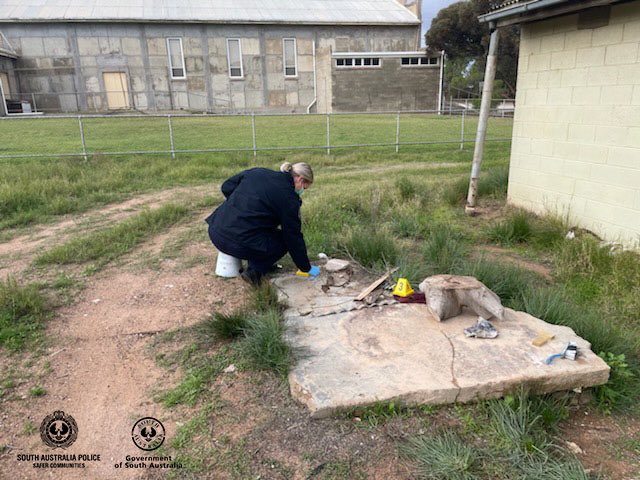 Police officer collecting evidence at Poochera art gallery near concrete block.
