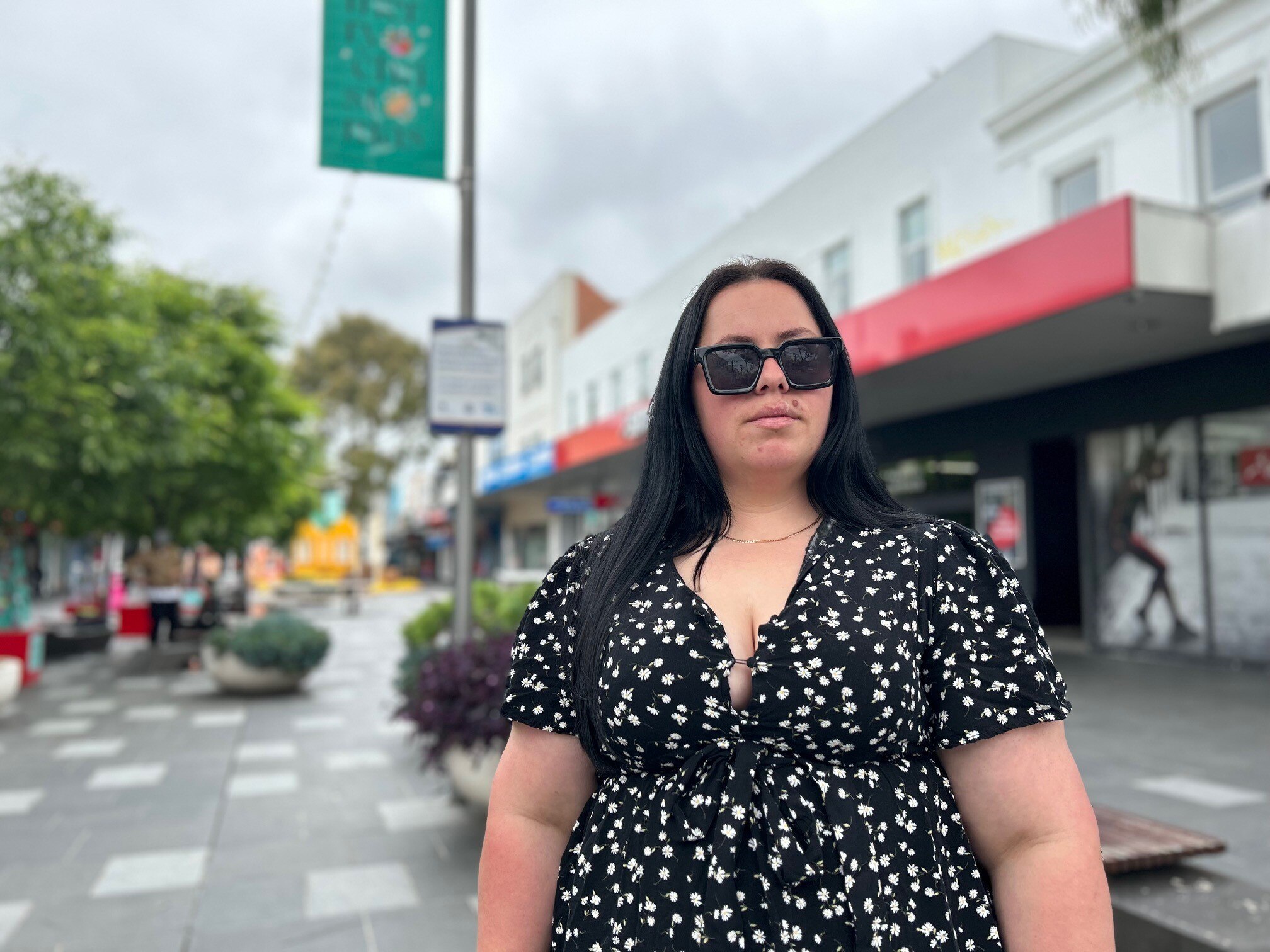 Woman in a black dress with printed white florals wearing sunglasses, standing on a street.
