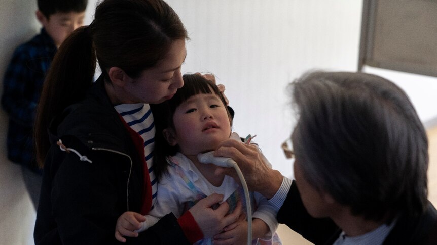 A doctor holds thyroid testing equipment to the throat of a small girl