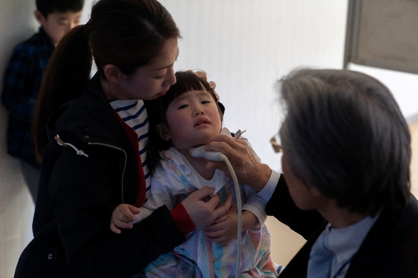 A doctor holds thyroid testing equipment to the throat of a small girl