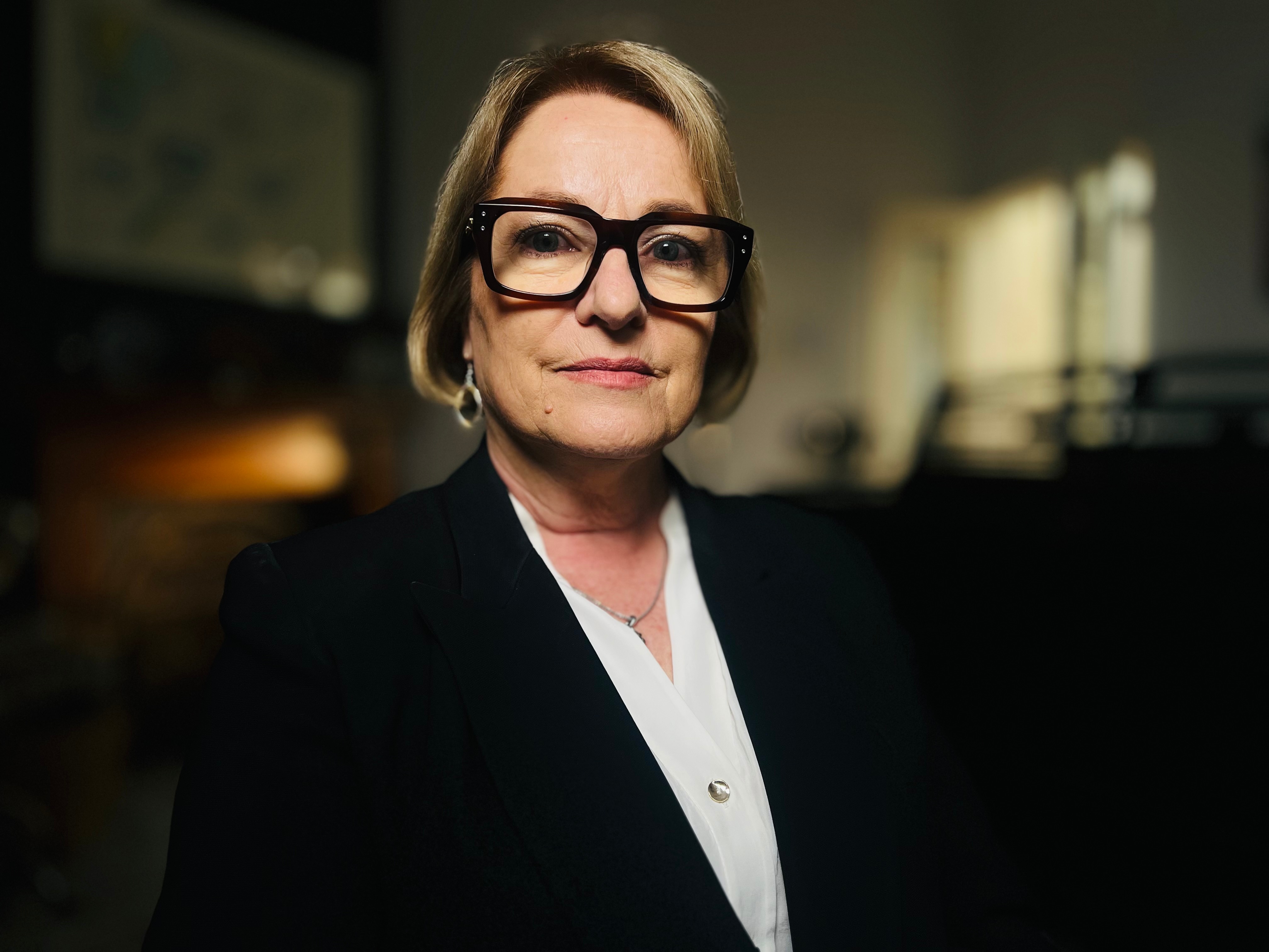 a middle-aged professional-looking woman wearing a dark blazer and reading glasses