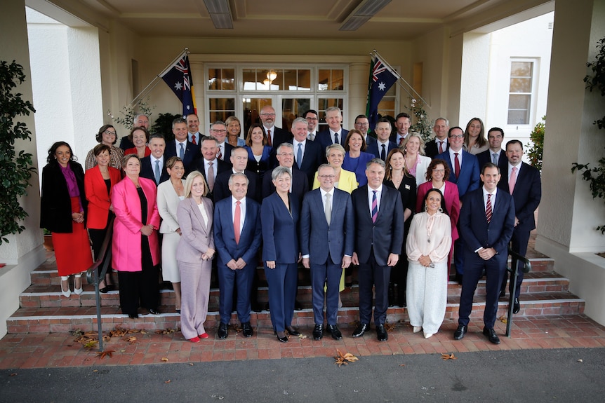 A group of politicians mostly in suit jackets poses for a photo on a small set of stairs