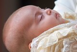 Close up shot of peaceful baby with eyes closed, wearing cream-coloured lace christening clothes