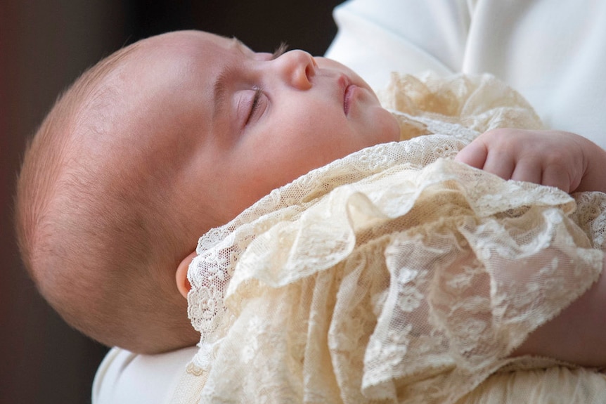 Close up shot of peaceful baby with eyes closed, wearing cream-coloured lace christening clothes
