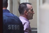 Jason Roberts arrives at the Supreme Court of Victoria wearing a pink collared shirt, accompanied by an SESG officer.