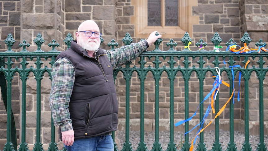 A man stands in front of a church fence