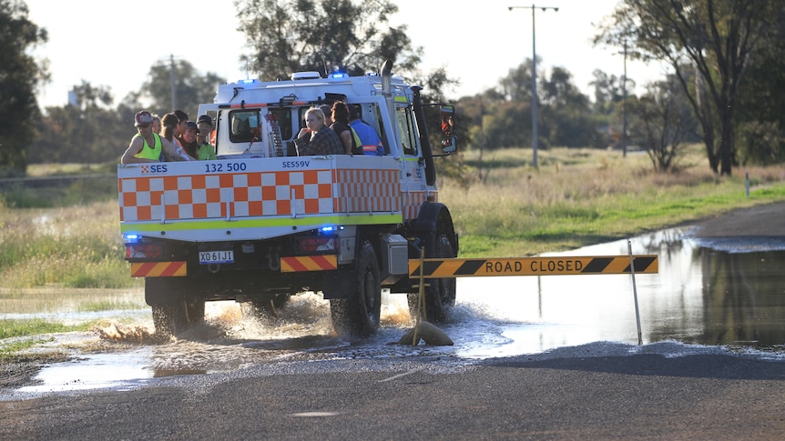People sitting in the back of an SES ute driving over a flooded road.