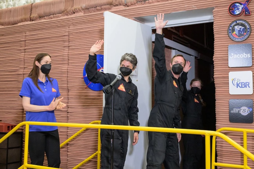 Three people in masks wave as they walk through a door