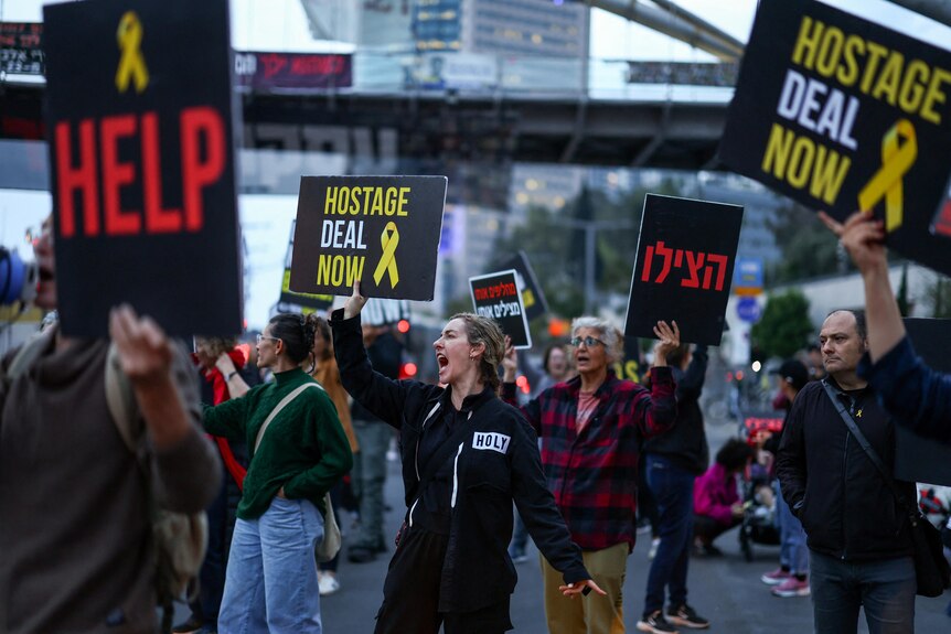 Protesters carry signs with messages including 'help' and 'hostage deal now' as well as Hebrew text