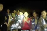 Spotlight shines on a group of boys wrapped in silver thermal blankets and a navy diver wearing black