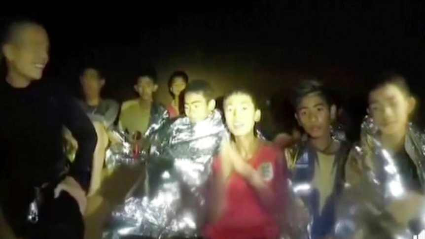 Spotlight shines on a group of boys wrapped in silver thermal blankets and a navy diver wearing black