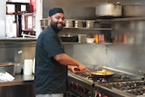 A man holding a pan cooking at a stove top in a commercial kitchen.