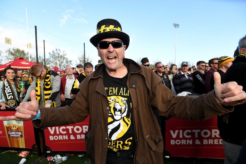A man does a thumbs up gesture and wears a tigers shirt and yellow and black top hat.