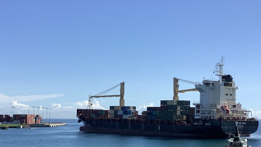 A large container ship is seen in the water near the mouth of an industrial port.