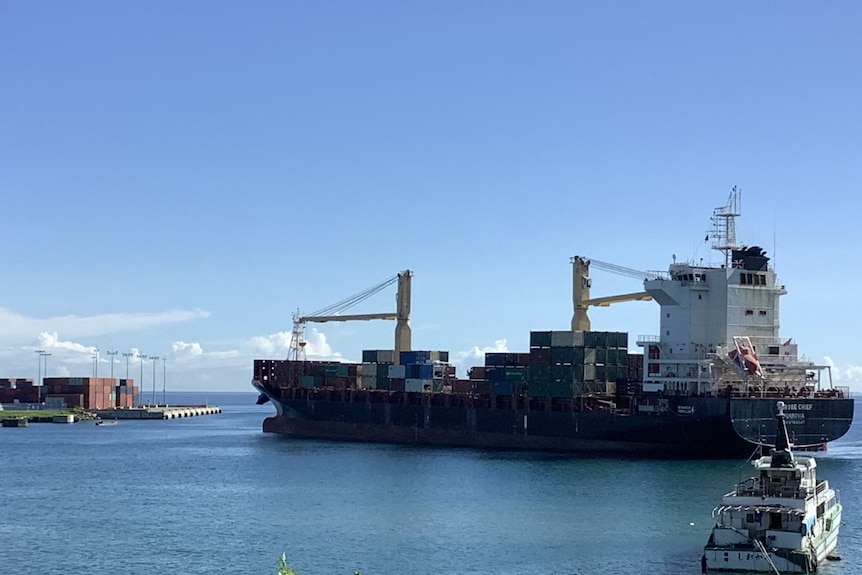 A large container ship is seen in the water near the mouth of an industrial port.