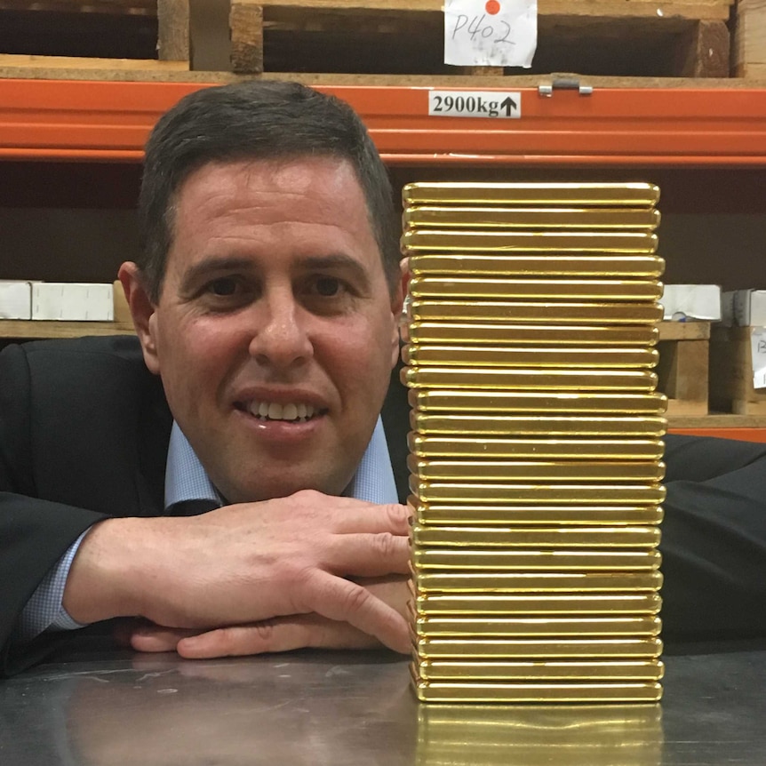 Perth Mint COO, David Woodford with arms folded on a table, next to a stack of 1 kilo 99.99 per cent pure gold bullion bars