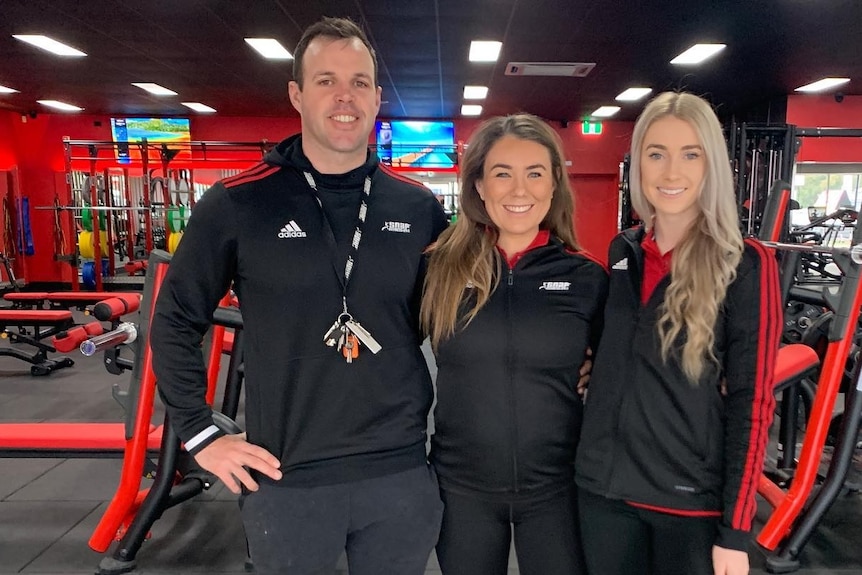 three people standing in a flash, red gym, smiling