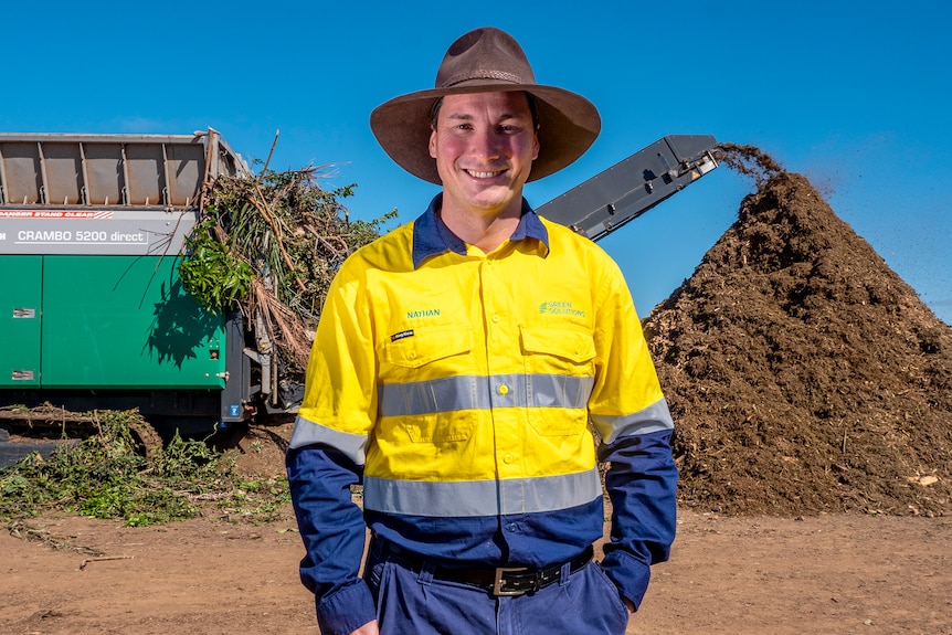 A man stands in front of a large machine grinding trees and shrubs.