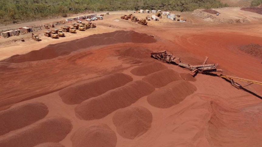 piles of iron ore on the ground, with machinery lined up in the background. 