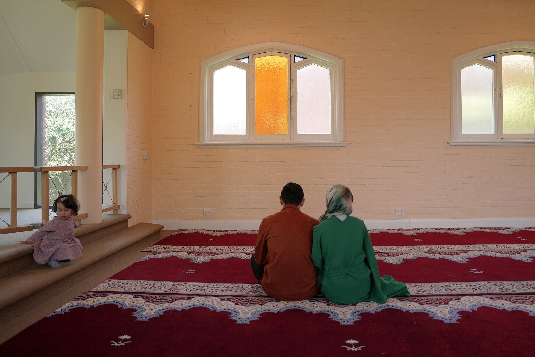 Una mujer con una abaya verde y un hiyab de seda bordado, un hombre con camisa y vaqueros y un niño de dos años caminan por la iglesia.