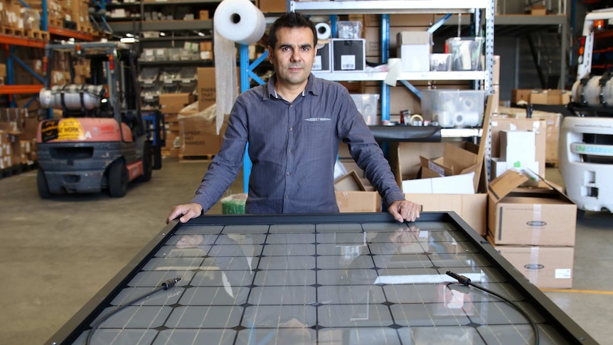 Durmus Yildiz leans on a large solar panel in his factory, with a forklift in the background.