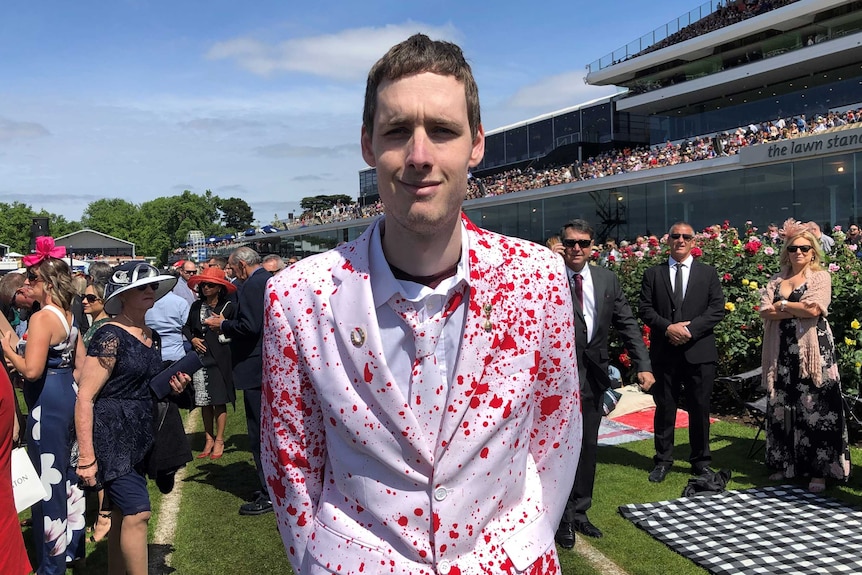 A man at the Melbourne Cup wearing a white suit with a blood splatter design.