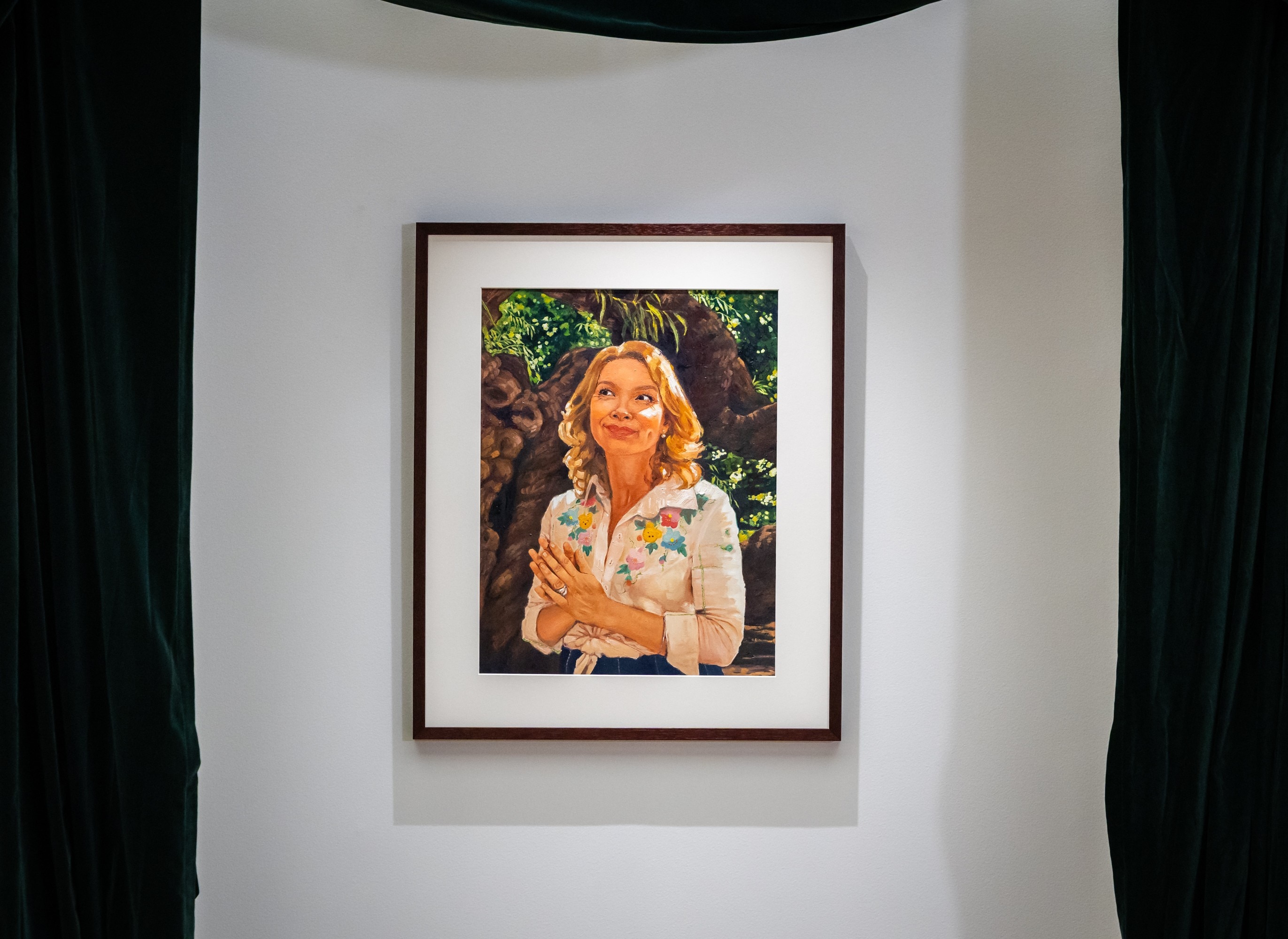 An oil painting of Justine Clarke standing under a tree with light on her face and hair
