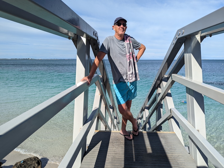Man wearing thongs, shirt and shorts stands on stairwell into ocean 