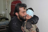 A man hugs his young son who has a bandaged wrapped around his head.