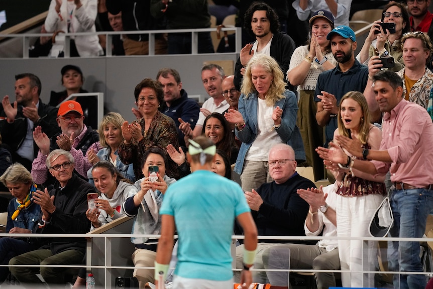 Fans at Roland Garros applaud Rafael Nadal, blurry on court in the foreground.