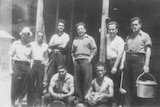 8 men in 1940s casual attire lean against wood hut in pow camp Nangwarry SA
