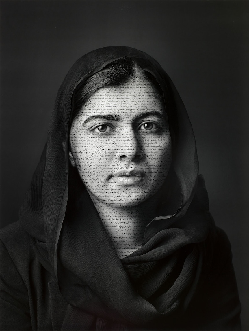 A black and white portrait of a woman with a scarf draped over her head, staring calmly at the viewer.