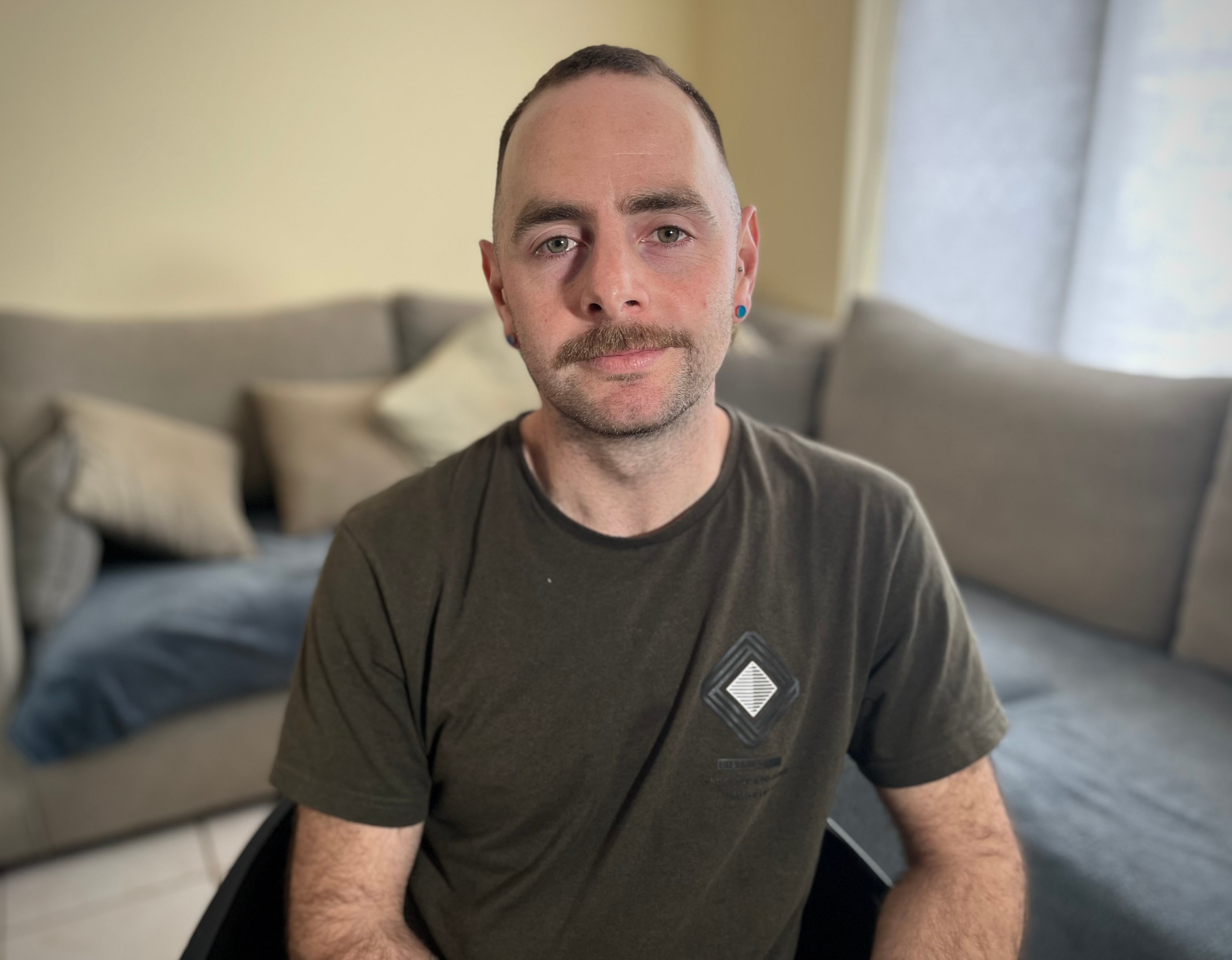 A man looking at the camera with a neutral expression with a lounge behind him