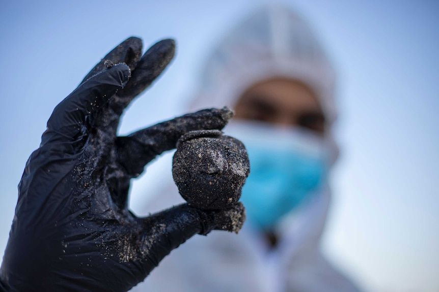 A man in protective gear holds up a glob of tar