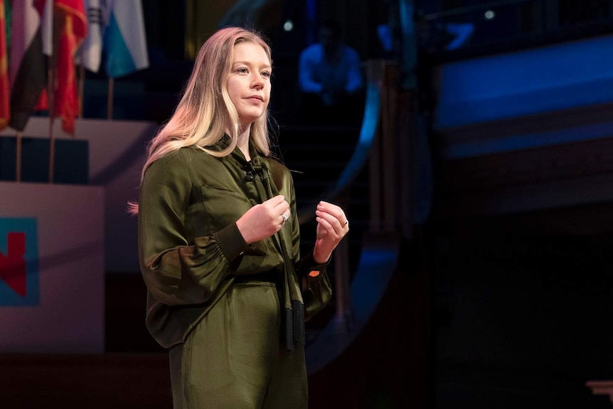 A woman stands on a stage addressing an audience.