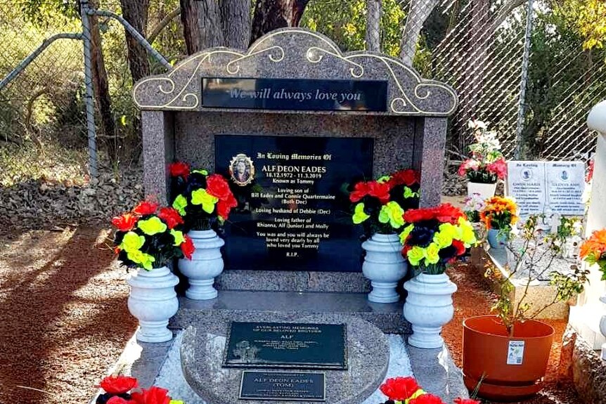 A grave surrounded by vases of flowers in the colours of the Aboriginal flag.