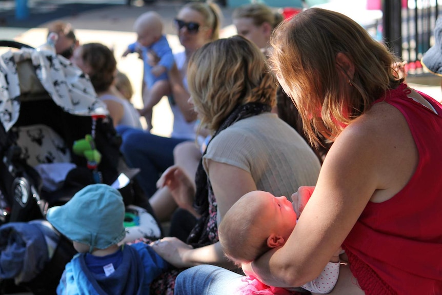 A baby looks up at its mum who prepares to breastfeed the baby.