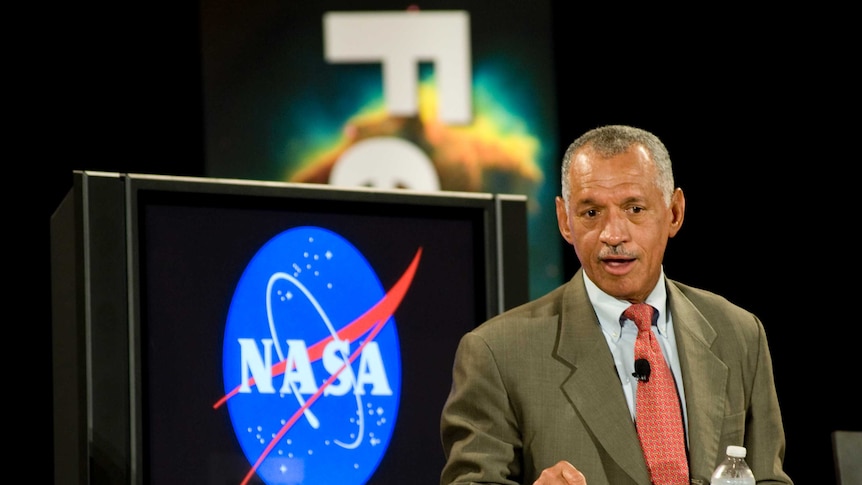 Charles Bolden, recently retired head of NASA talks in front of a TV screen with the NASA logo displayed.