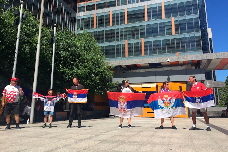 A group of six people stand outside a court complex with Serbian flags