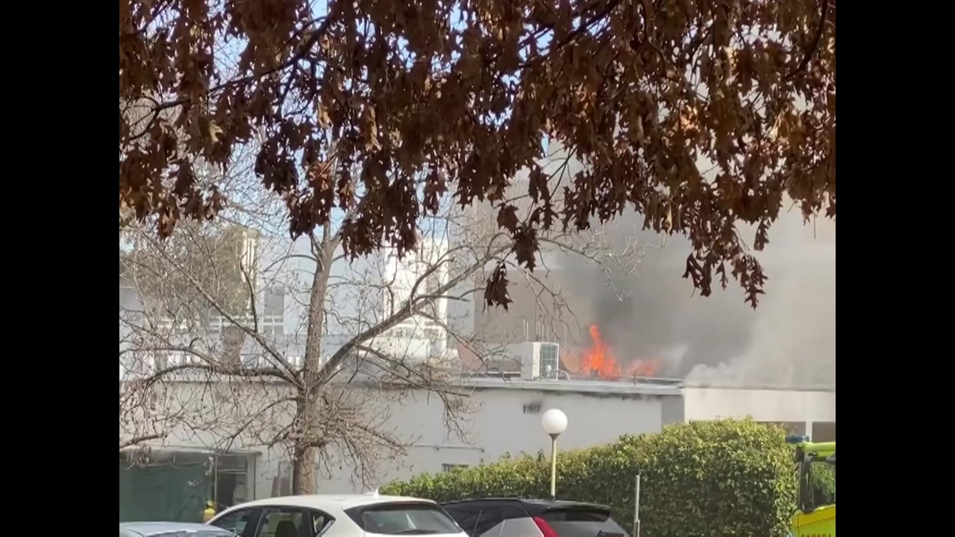 A large building on fire surrounded by treeswith orange leaves.