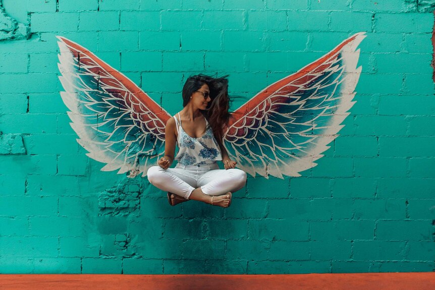 A woman jumping against a pair of wings painted on a wall to illustrate an enduring guardian