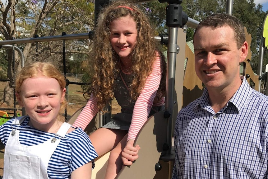 Peter Garvey with his two daughters, who are sitting on a slippery dip at a playground