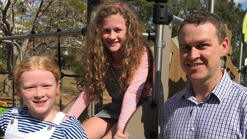 Peter Garvey with his two daughters, who are sitting on a slippery dip at a playground