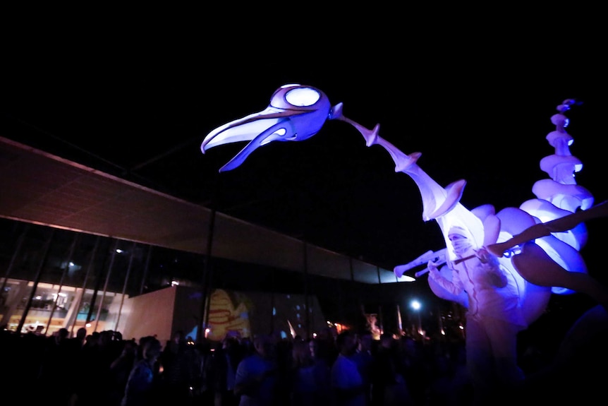 A person holds a glowing bird as it walks through a crowd at White Night.