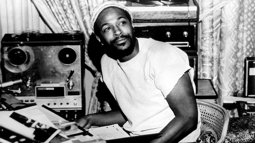 A black and white 70s photo of a Black man, Marvin Gaye in a studio he looks to one side and smiles