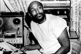 A black and white 70s photo of a Black man, Marvin Gaye in a studio he looks to one side and smiles