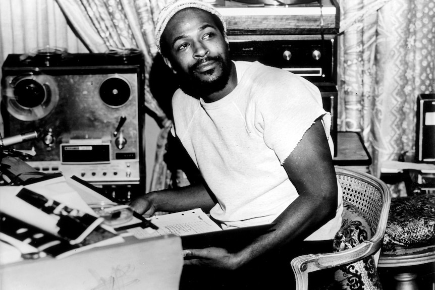 A black and white 70s photo of a Black man, Marvin Gaye in a studio he looks to one side and smiles